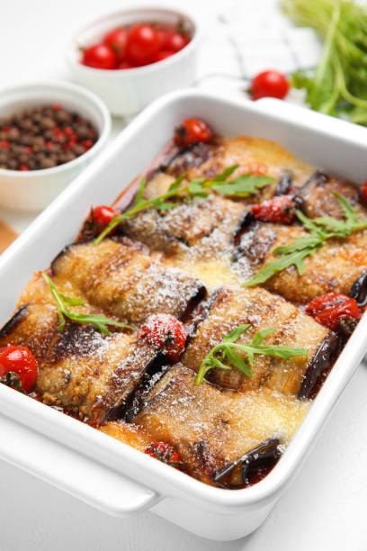 istock Tasty eggplant rolls with tomatoes, cheese and arugula in baking dish on white table, closeup 1403028851