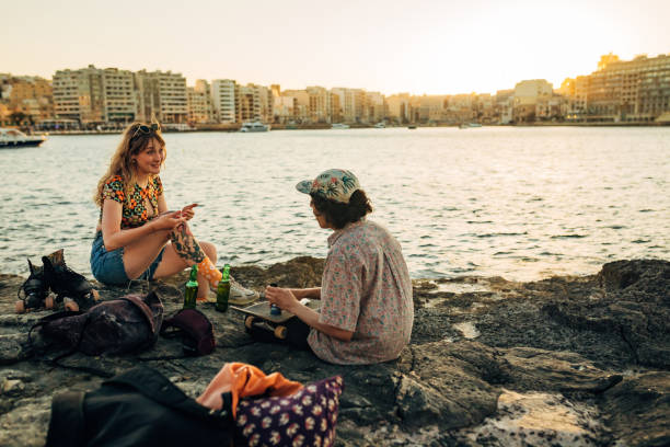 istock Two cheerful skaters sitting on a rocky shore, smoking a joint and drinking a cold, refreshing beer 1403028955