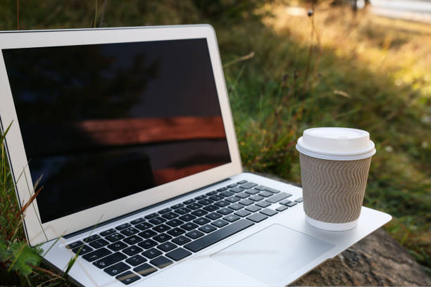 istock Modern laptop with blank screen and coffee cup on stone in nature, space for text. Working outdoors 1403029982