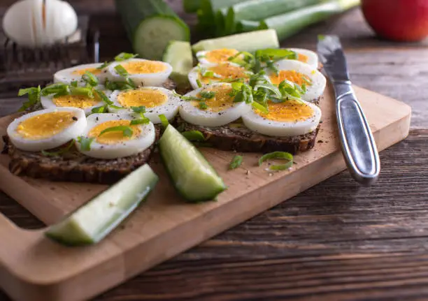 Vegetarian sandwich meal with fresh cooked boiled egg, whole grain bread. Topped with pepper, salt and chives. Served on wooden table background. Ready to eat