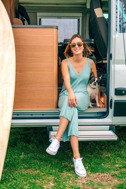 mujer sentada con su perro en la puerta de su autocaravana durante un viaje - poco chica divertida con gafas de sol en el césped en verano fotografías e imágenes de stock