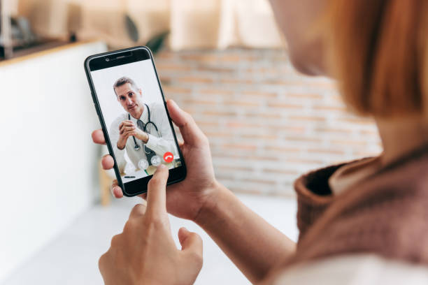 Young woman meet her doctor via video call by smart phone at home. stock photo