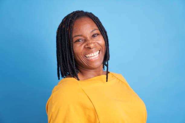 portrait of smiling black woman in yellow sweater isolated on blue background stock photo