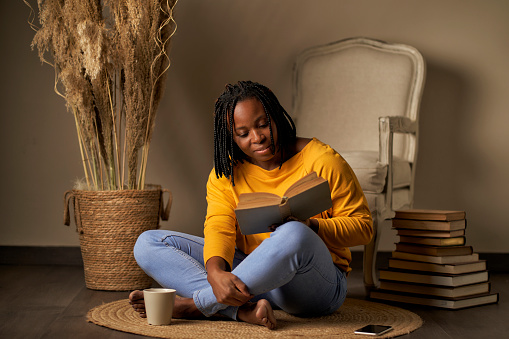 a black woman reading a book while sitting on a rug
