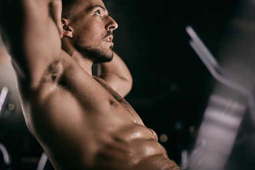 Muscular build sportsman exercising sit-ups in a gym.