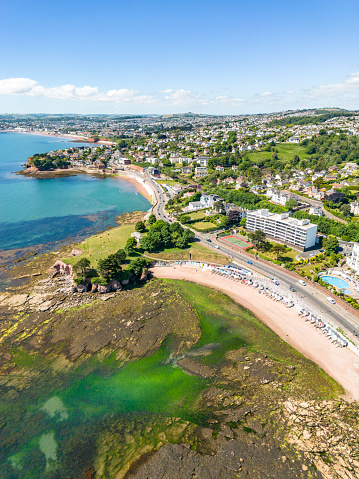 Torquay, UK. Tuesday 14 June 2022. Seafront houses, beach huts and headland in Torquay with people on the beach.