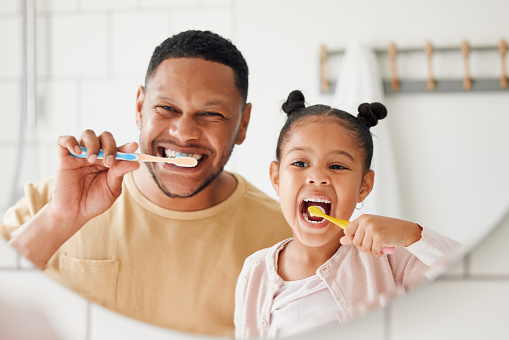 Feliz padre e hija mestizos cepillándose los dientes juntos en un baño de casa. Padre afroamericano soltero enseñando a su hija a proteger sus dientes photo
