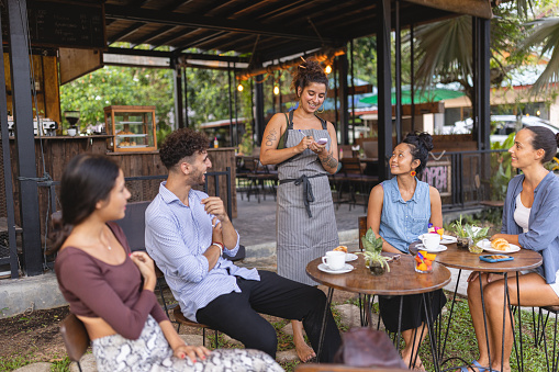 Caucasian waitress taking orders of the multiracial customers, at the coffee shop