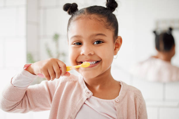 una adorable niña de raza mixta cepillándose los dientes en un baño de casa. un niño hispano feliz con hábitos diarios saludables para prevenir caries y fortalecer el esmalte - cepillar los dientes fotografías e imágenes de stock