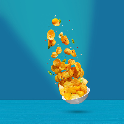 Tasty potato chips falling onto plate on colorfull background. Levitation flying potato chips with salt and peppers. Advertising concept.