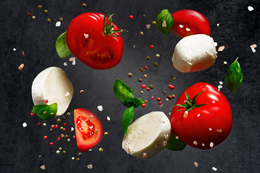 Falling caprese salad ingredients on dark background. Falling mozzarella cheese and tomatoes on dark background