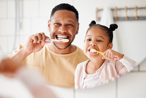 Feliz padre e hija mestizos cepillándose los dientes juntos en un baño de casa. Padre afroamericano soltero enseñando a su hija a proteger sus dientes photo