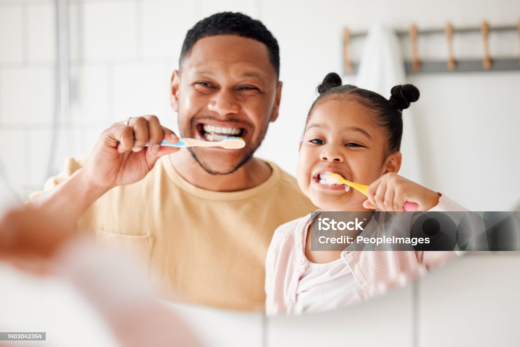 Happy mixed race father and daughter brushing their teeth together in a bathroom at home. Single African American parent teaching his daughter to protect her teeth Dental Health Stock Photo