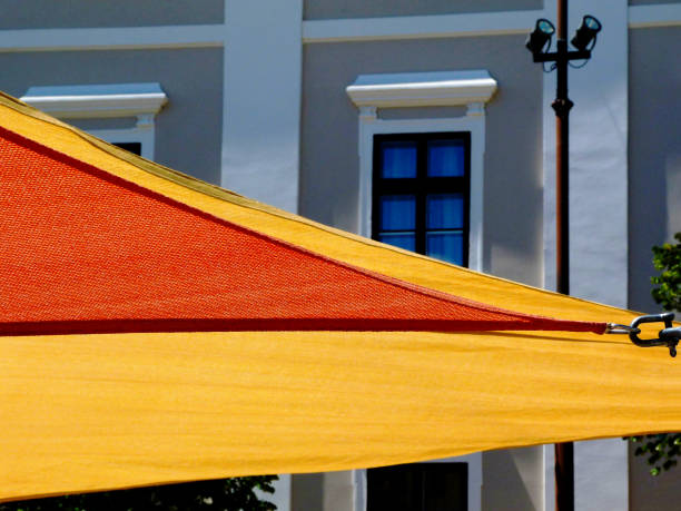 gelbe und orangefarbene sonnenschutzmarkisen aus segeltuch über kopf. stuckfassaden dahinter. - shade sail awning textile stock-fotos und bilder