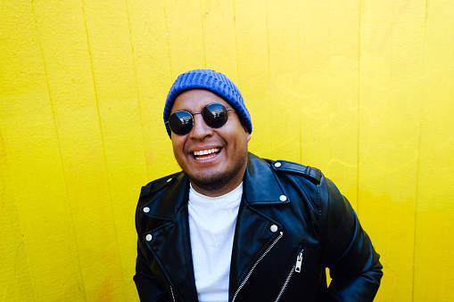 Close-up of smiling mid adult man standing against yellow wall with sunglasses and beanie