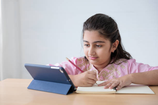 istock cute Indian girl writing on notebook and looking tablet for online learning class, education concept 1403043849