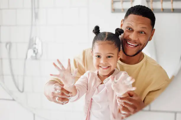 Photo of Happy mixed race father and daughter washing their hands  together in a bathroom at home. Single African American parent teaching his daughter about hygiene while having fun and being playful