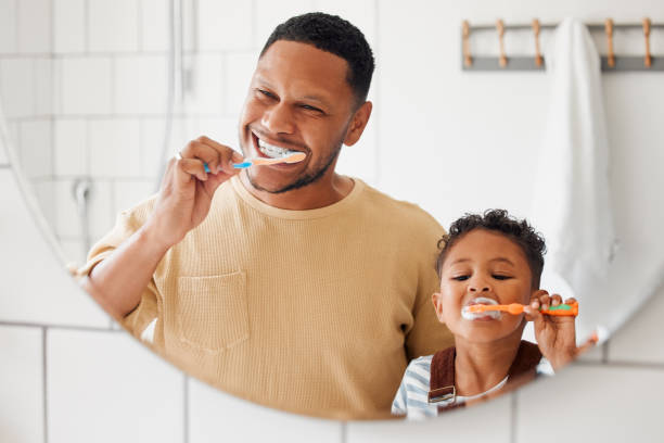 幸せな混血の父と息子は、自宅のバスルームで一緒に歯を磨いています。アフリカ系アメリカ人の独身の親が息子に歯を守るように教える - 歯みがき ストックフォトと画像