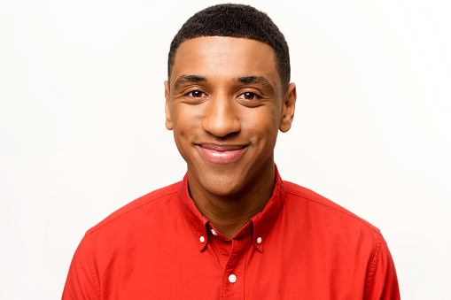 Headshot of friendly optimistic African-American guy in red shirt isolated on white. Smiling kind male student looking at the camera, portrait of employee