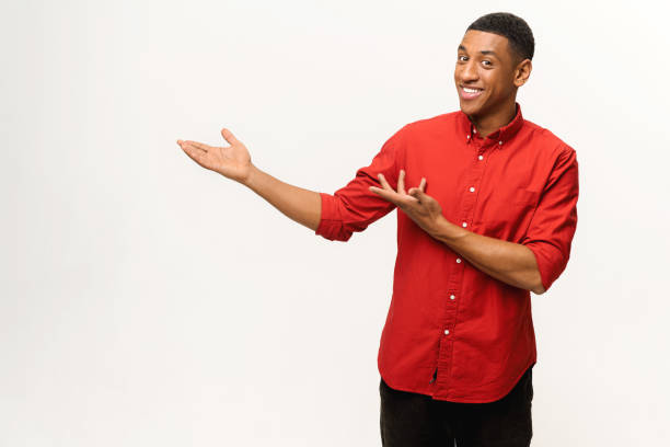 Handsome African-American young man in red shirt points palms aside isolated on white