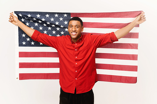 Cheerful African-American guy holding in hands spreaded american flag isolated over white background, multiracial foreign student man holding US flag, independence day celebration, holiday