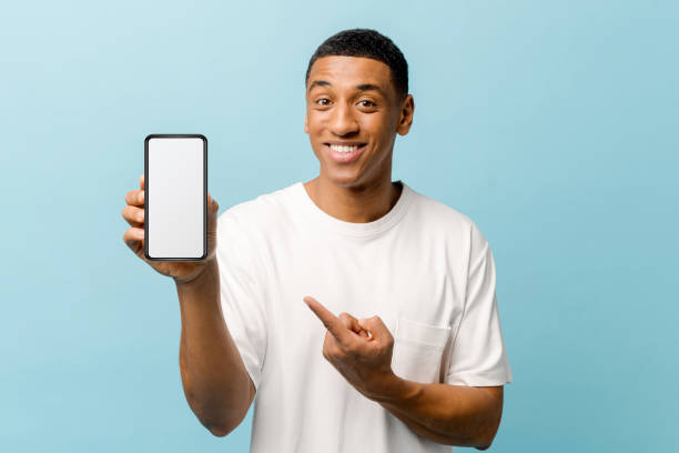 istock Smiling African-American young guy points index finger at empty smartphone screen 1403045878