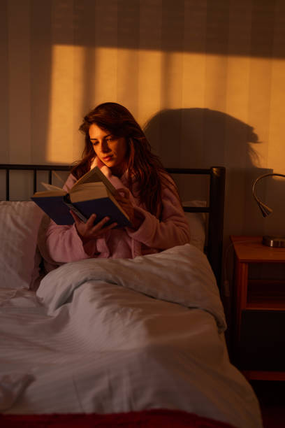 istock Young woman reading a book while relaxing on a bed. 1403047478