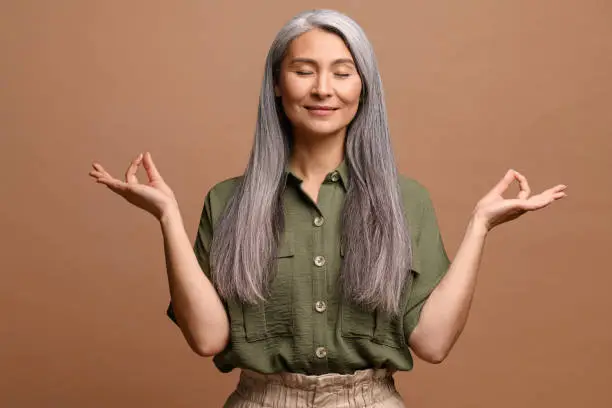 Photo of Meditation concept. Calm and satisfied mature woman holds her hands in zen gesture, keeps eyes closed, feels appeasement and pacification, practicing yoga