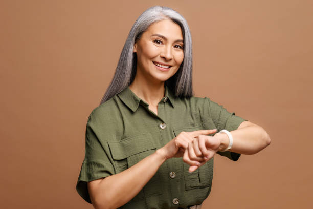 belle femme asiatique mature aux cheveux gris portant des vêtements décontractés pressé de pointer du doigt l’heure de regarder, l’impatience, parler de la date limite - vérifier lheure photos et images de collection