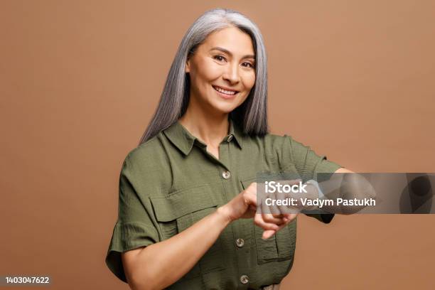 Mature Beautiful Asian Woman With Grey Hair Wearing Casual Clothes In Hurry Pointing To Watch Time Impatience Talking About Deadline Stock Photo - Download Image Now