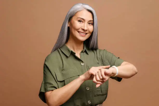 Photo of Mature beautiful asian woman with grey hair wearing casual clothes In hurry pointing to watch time, impatience, talking about deadline