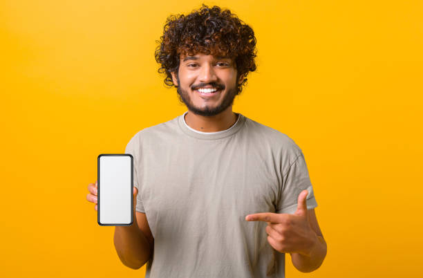 istock Positive happy Indian man showing smartphone with white empty display, points finger on it 1403048595