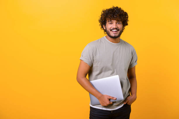 istock Cheerful Indian young man holding laptop standing isolated on yellow 1403048629