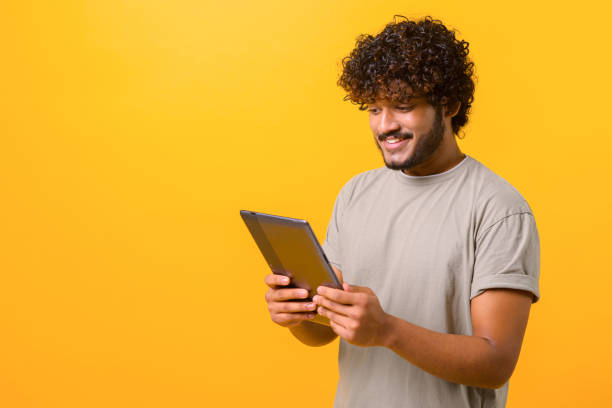 istock Smiling handsome Indian young curly man reading electronic book 1403048632