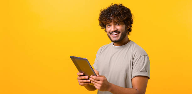 istock Cheerful young Indian man holding digital tablet isolated on yellow 1403048638