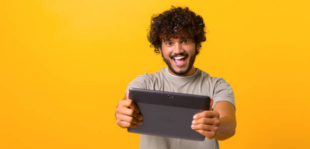 istock Excited curly young Indian man playing video game on the digital tablet 1403048643
