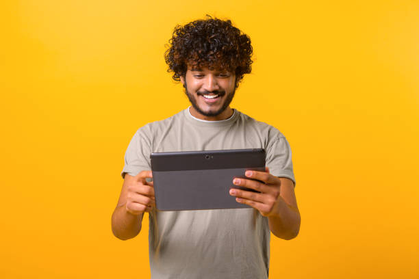 istock Positive handsome Indian young curly man using digital tablet for web surfing or remote working 1403048649