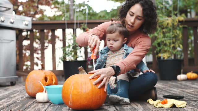 Cute Eurasian toddler carving jack o' lantern pumpkin with her mom