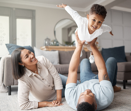 A happy mixed race family of three relaxing on the lounge floor and being playful together. Loving black family bonding with their son while playing fun games on the carpet at home