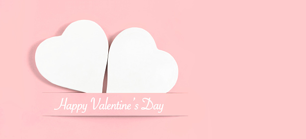 White heart shaped ornaments on pastel pink background with copy space and Valentine’s Day message