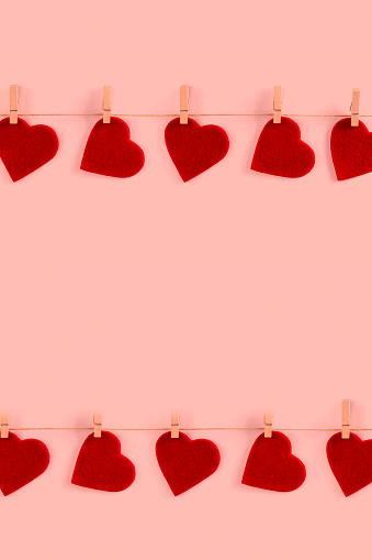 Valentine background with red felt hearts on clothespins on pink background
