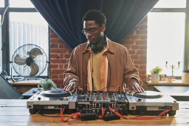 istock Young black man in casualwear looking at dj board while touching turntables 1403054810