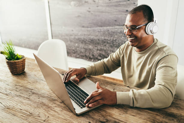 istock Senior african man using laptop computer while wearing headphones at home - Focus on face 1403056058