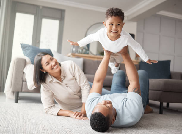 eine glückliche gemischtrassige familie von drei personen, die sich auf der lounge-etage entspannen und zusammen verspielt sind. liebe schwarze familie, die sich mit ihrem sohn verbindet, während sie zu hause lustige spiele auf dem teppich spielen - parent playful father mother stock-fotos und bilder