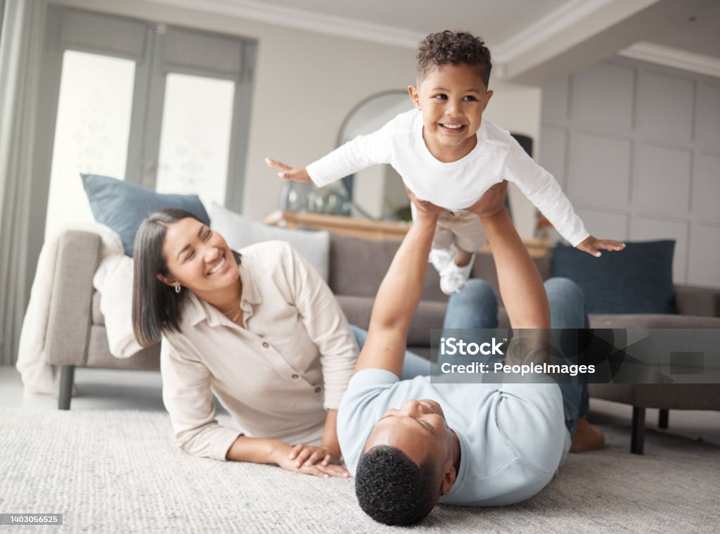 A happy mixed race family of three relaxing on the lounge floor and being playful together. Loving black family bonding with their son while playing fun games on the carpet at home Family Stock Photo