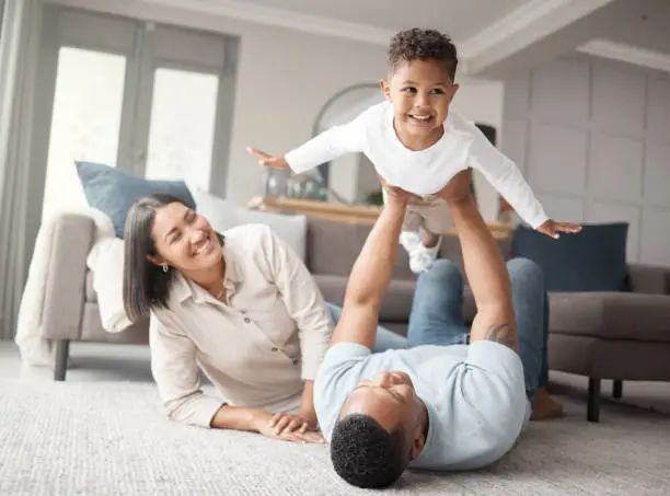 Photo of A happy mixed race family of three relaxing on the lounge floor and being playful together. Loving black family bonding with their son while playing fun games on the carpet at home