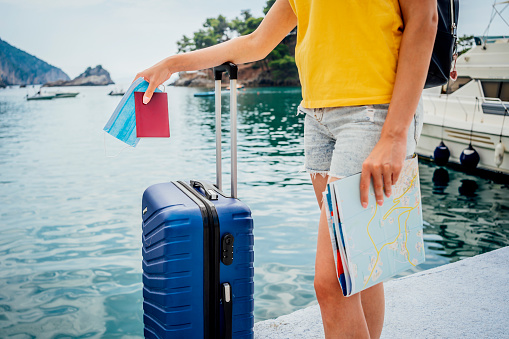 Woman holding passport, map and luggage bag by the sea