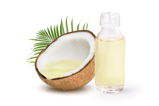 Coconut oil in glass bottle and coconut fruit with green leaves isolated on white background.