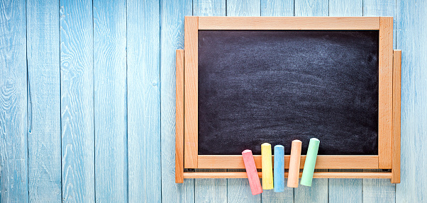 Small black board with colored chalks on blue wooden planks. Back to school concept.