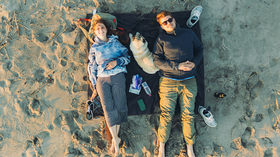 Drone panoramic photo of a smiling couple with cute pug relaxing by the beach surrounded by the waved sea and the sand dunes in Patara, Turkish Riviera